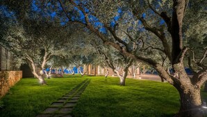 A pathway leading through a well-maintained garden with trees and a stone wall on one side. - Villa Zenais, Luxury with swimming pool (Koridallos)