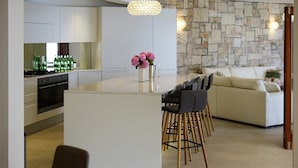 A modern kitchen with a central island, bar stools, a stone accent wall, and a cozy seating area. - Villa Josipa - Luxury modern villa with pool in Croatia (Puntinak)