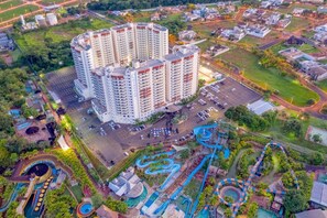 Een hoog hotel met meerdere verdiepingen, een parkeerplaats en een aangelegde omgeving met paden en een waterpartij.