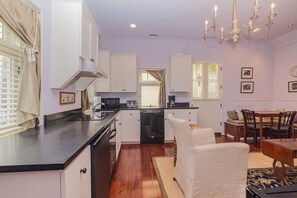 Cocina compacta con armarios blancos, encimera negra y zona de comedor con mesa y sillas de madera.