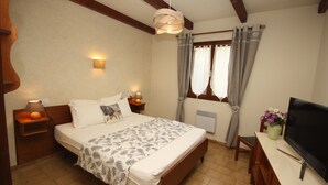 A bedroom with a bed, bedside lamps, a desk with a TV, and a window with curtains. - Villa Castagna Dans un Splendide Parc Fleuri, Calme à 900 m de la Plage (Calvi)