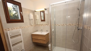 A bathroom with a glass-enclosed shower, a sink with a mirror above it, and a towel rack. - Villa Castagna Dans un Splendide Parc Fleuri, Calme à 900 m de la Plage (Calvi)