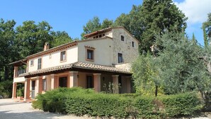 A two-story house with a tiled roof, surrounded by greenery and trees.