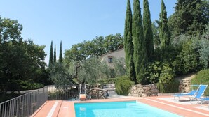 A swimming pool with lounge chairs, surrounded by tall cypress trees and a stone wall.