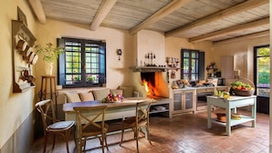 Una cocina rústica con un horno de leña central, muebles de madera y vistas al exterior a través de amplias ventanas.