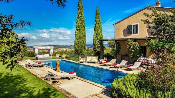 Un área de piscina con sillas de descanso y una pérgola, rodeada de vegetación y vistas al campo.