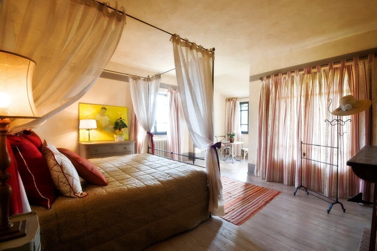 Een slaapkamer met een bed, gordijnen, een lamp, een schilderij en een raam.