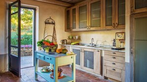 Una cocina rústica con armarios de madera, una mesa azul y vistas al verdor exterior.