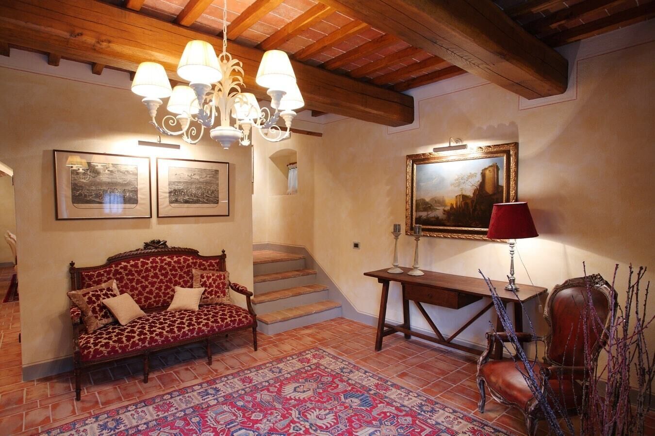 Un salon chaleureux avec un canapé à motifs, une table basse en bois, une lampe rouge et un escalier menant à un autre niveau.