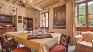 Een eetkamer met een tafel gedekt voor vier personen, een kroonluchter en een schilderij aan de muur.