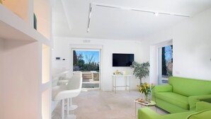 A modern living room with a green sofa, white chairs, a small table with a vase, and a TV mounted on the wall. - Resort Lubrense - Mandragola with pool and jacuzzi (Sant'Agata Sui Due Golfi)