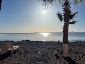 Ein Strand mit einer Palme, einer Liege und einer felsigen Küstenlinie.