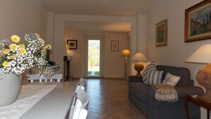 A living room with a sofa, a dining table with chairs, a large vase of flowers, and a door leading to another room.