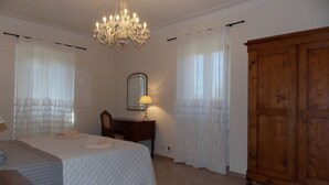 A bedroom with a bed, a wooden wardrobe, a desk with a mirror, and a chandelier.