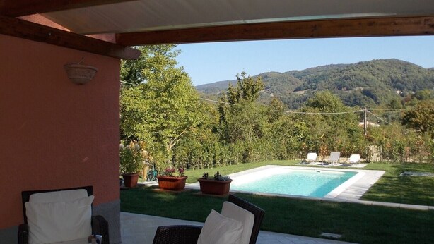 A pool area with a view of mountains, surrounded by potted plants and outdoor furniture.
