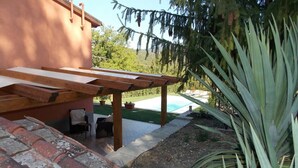 A covered patio area with a pool, outdoor furniture, and a view of a lush garden.