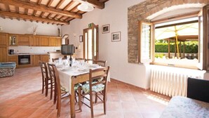 Uma sala de jantar com uma mesa de madeira posta para quatro pessoas, uma parede de pedra e vista para o verde lá fora.