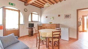 Uma sala de estar acolhedora com sofá, mesa de jantar com cadeiras, televisão e área de cozinha com armários e geladeira.