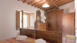 Quarto com cama de madeira, cômoda, espelho e janela com cortinas.