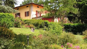 A yellow house with a red roof, surrounded by lush greenery and flowering plants.