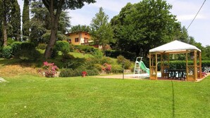 A well-maintained garden with a gazebo, a playground, and a house in the background.