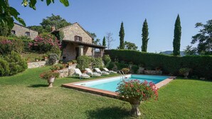 Ein Pool mit Liegestühlen, ein Steinhaus und ein gepflegter Garten.