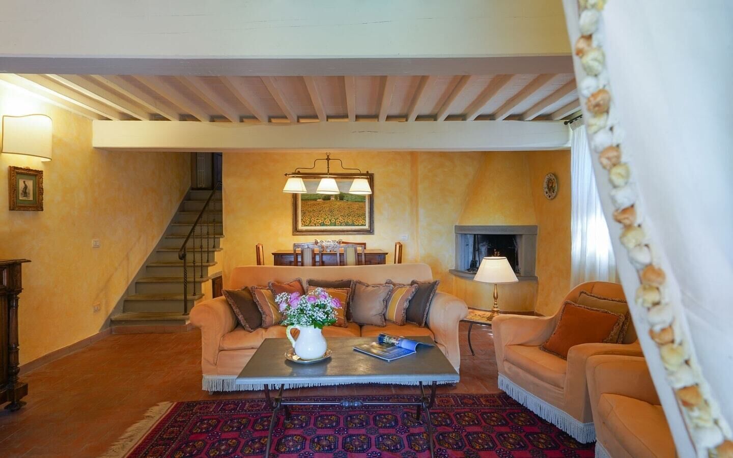 Uma sala de estar com sofá, mesa de centro e lareira. Escada visível ao fundo.