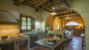Una cocina rústica con vigas de madera, una chimenea de piedra y un comedor con una mesa dispuesta para dos.