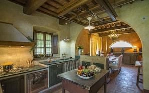 A rustic kitchen with wooden beams, a stone fireplace, and a dining area with a table set for two. - Villa Nami - Private villa with pool in Tuscany (Castiglion Ubertini)