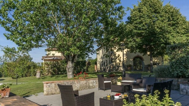 Un patio al aire libre con mobiliario de mimbre, un muro de piedra y un edificio al fondo.