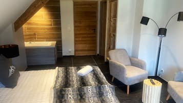 Un dormitorio moderno con techo inclinado, bañera integrada, un sillón gris, una lámpara de pie y una mesa de centro original.