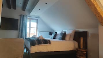 Ein Schlafzimmer mit Bett, Sessel, Holz-Kopfteil, Fenster und einem angebrachten Fernseher.