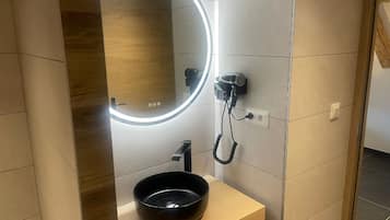 A bathroom with a modern design, featuring a wooden vanity, a black sink, a hairdryer, and a mirror with a lighted frame.