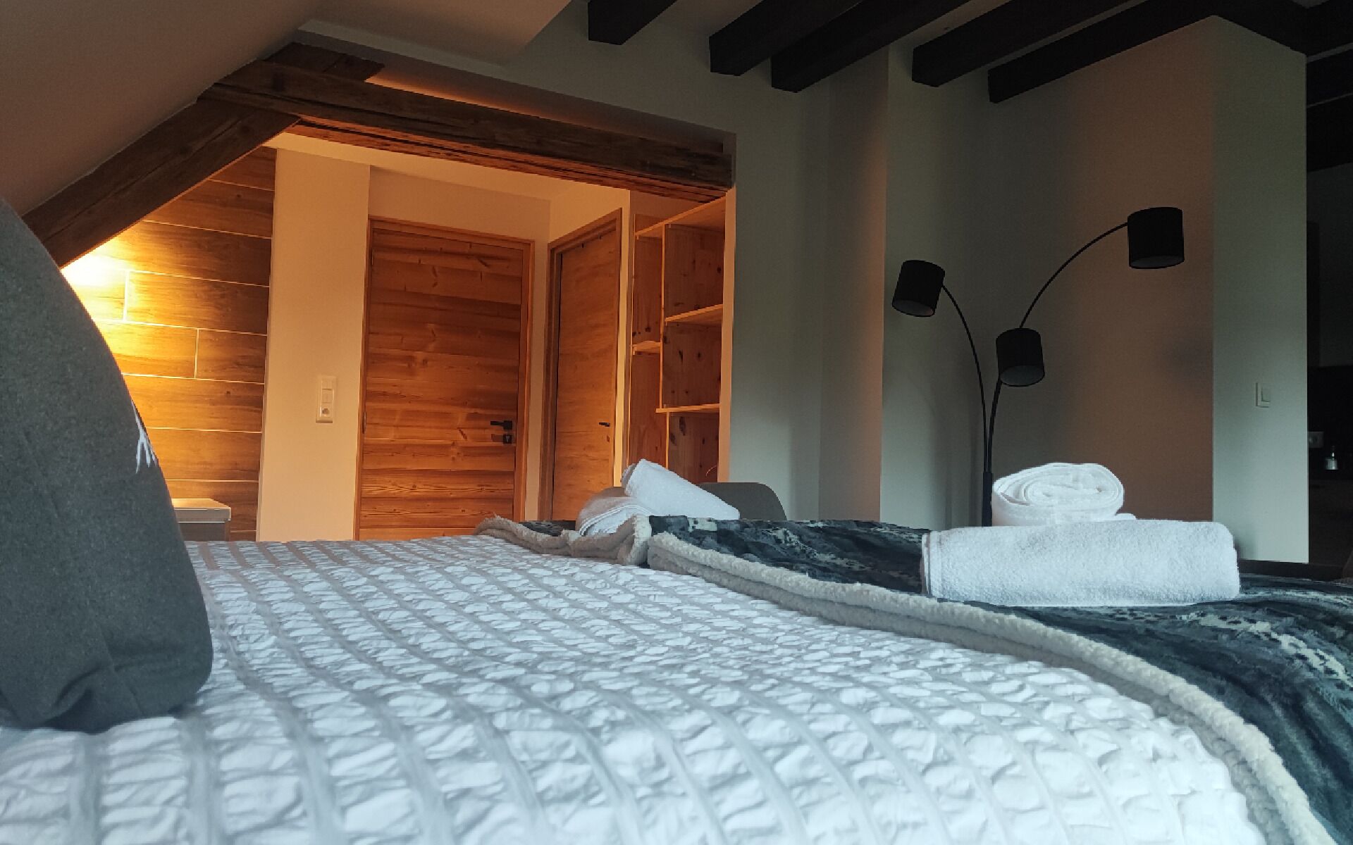 Ein Schlafzimmer mit Holzbalkendecke, einem Bett mit weißer Bettdecke, einem Holzschrank und einem Nachttisch mit Lampe.