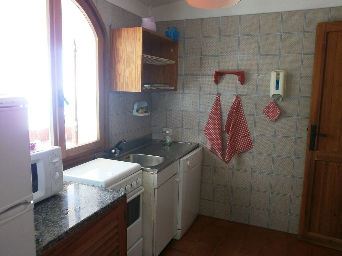 Cocina compacta con microondas, estufa, lavamanos y armarios de madera.