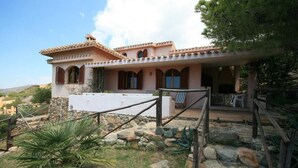 A Mediterranean-style house with a stone facade, a covered patio with outdoor furniture, and a view of the surrounding landscape. - Villa Mavriana - Private villa with sea views (Torre Delle Stelle (Maracalagonis))