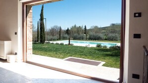 A view through a large glass door to a swimming pool, surrounded by a grassy area and trees.