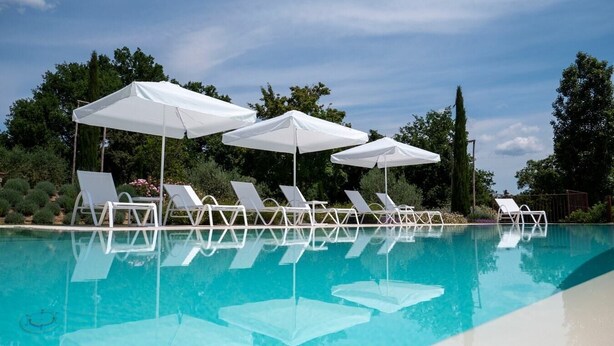 A swimming pool with white lounge chairs and umbrellas, surrounded by greenery.
