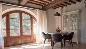 A dining area with a round table, four chairs, a fruit bowl, and a cabinet with glass doors.