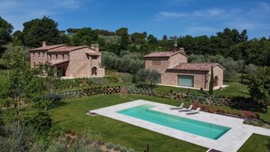 A villa with a swimming pool, surrounded by lush greenery and two brick buildings.