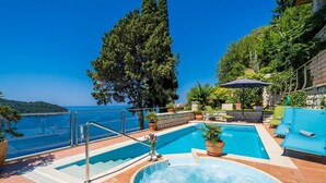 A pool area with a hot tub, lounge chairs, and a view of the sea.