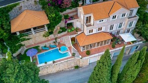A multi-story house with a swimming pool, outdoor seating, and a garden.