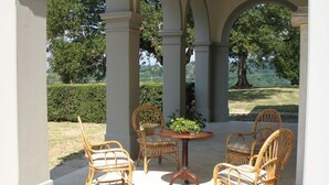 An outdoor patio with wicker chairs and a table, surrounded by white columns. - Villa Betti - Private villa with pool in Tuscany (Dicomano)