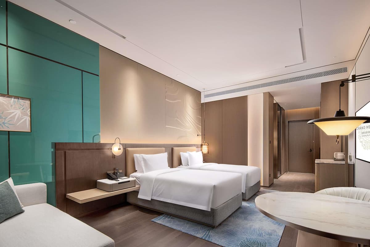 A modern hotel room with a bed, bedside tables, a desk, and a chair.
