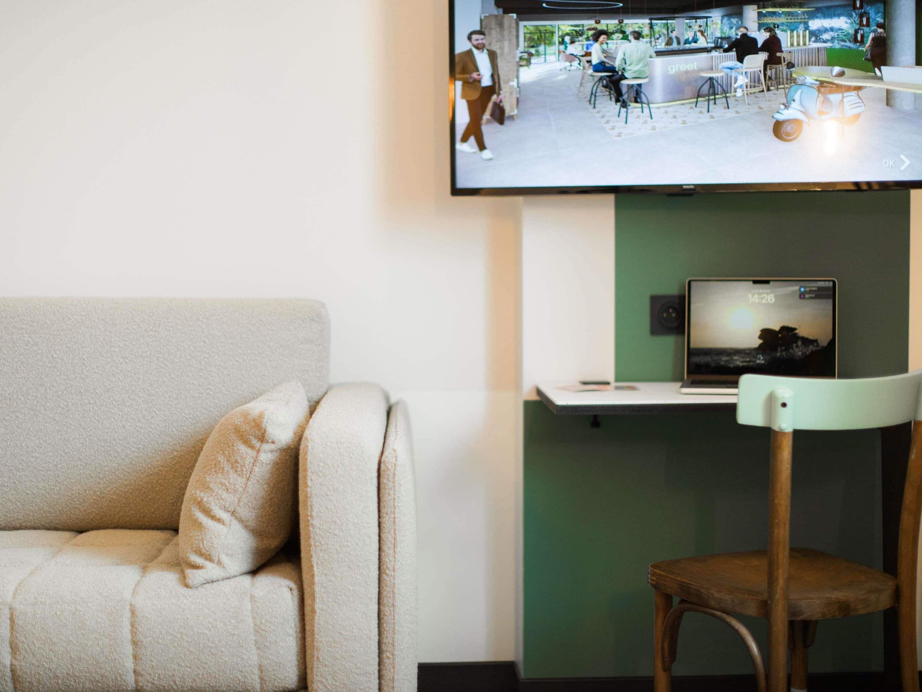 Un salon moderne avec un canapé, une chaise en bois, un téléviseur à écran plat fixé au mur et un ordinateur portable posé sur un support.