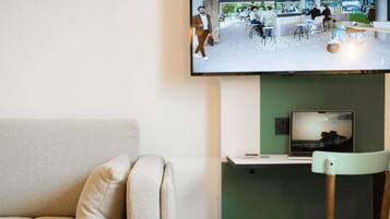 Un salon moderne avec un canapé, une chaise en bois, un téléviseur à écran plat fixé au mur et un ordinateur portable posé sur un support.