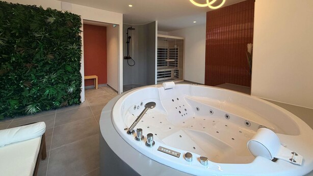 A modern bathroom with a freestanding bathtub, a shower area, and a green wall with plants. - Greet Hotel Brest Aéroport (Guipavas)