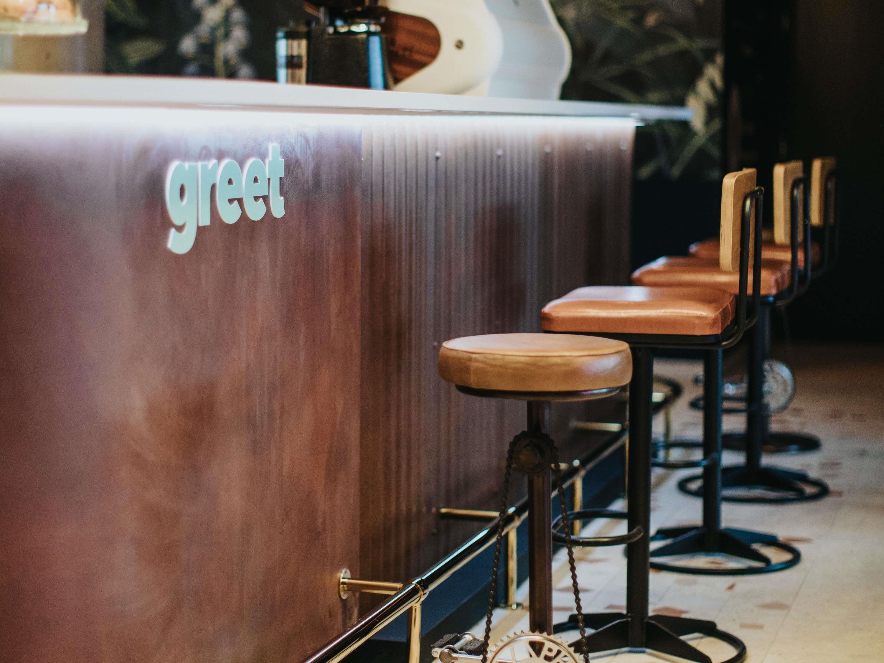 A bar area with a counter labeled 'greet' and several bar stools.