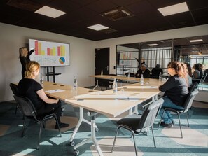 Une salle de conférence dotée d’une grande table, de chaises, d’un tableau blanc avec des graphiques, et offrant une vue sur l’extérieur grâce à de grandes fenêtres.