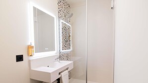 A modern bathroom with a white vanity, a glass shower enclosure, and a mirror above the sink. - Greet Hotel Brest Aéroport (Guipavas)